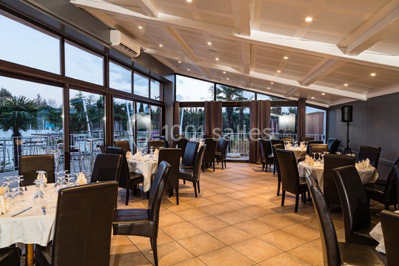 Salle de restaurant lumineuse avec grandes baies vitrées, tables dressées et vue sur une terrasse extérieure.