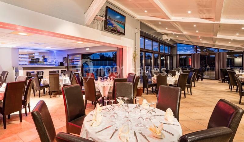 Salle de restaurant lumineuse avec tables rondes dressées, chaises en cuir sombre et grandes baies vitrées donnant sur l…
