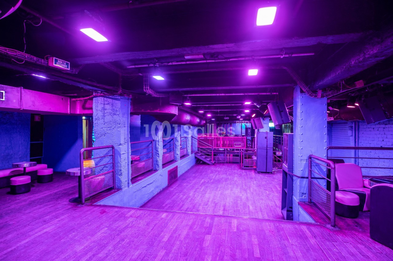 Salle vide d'une discothèque avec éclairage violet, murs bleus, piste en bois et mobilier minimaliste.