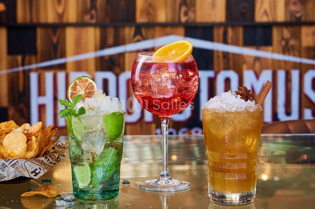 Trois cocktails colorés garnis de fruits et d'herbes, posés sur un comptoir avec des chips en arrière-plan.