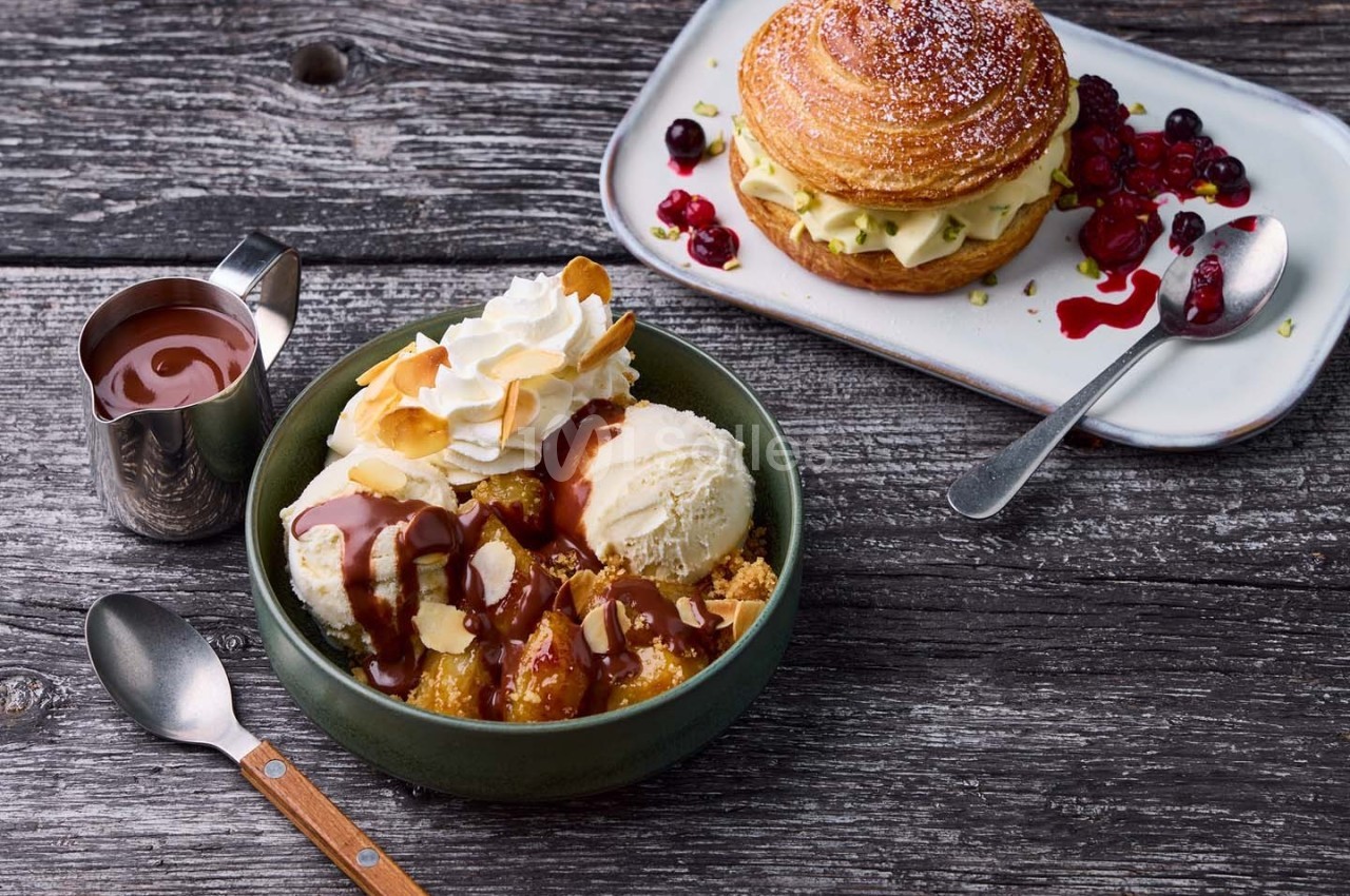 Dessert composé de glace vanille, chantilly, sauce chocolat, amandes grillées, avec une viennoiserie et fruits rouges en…