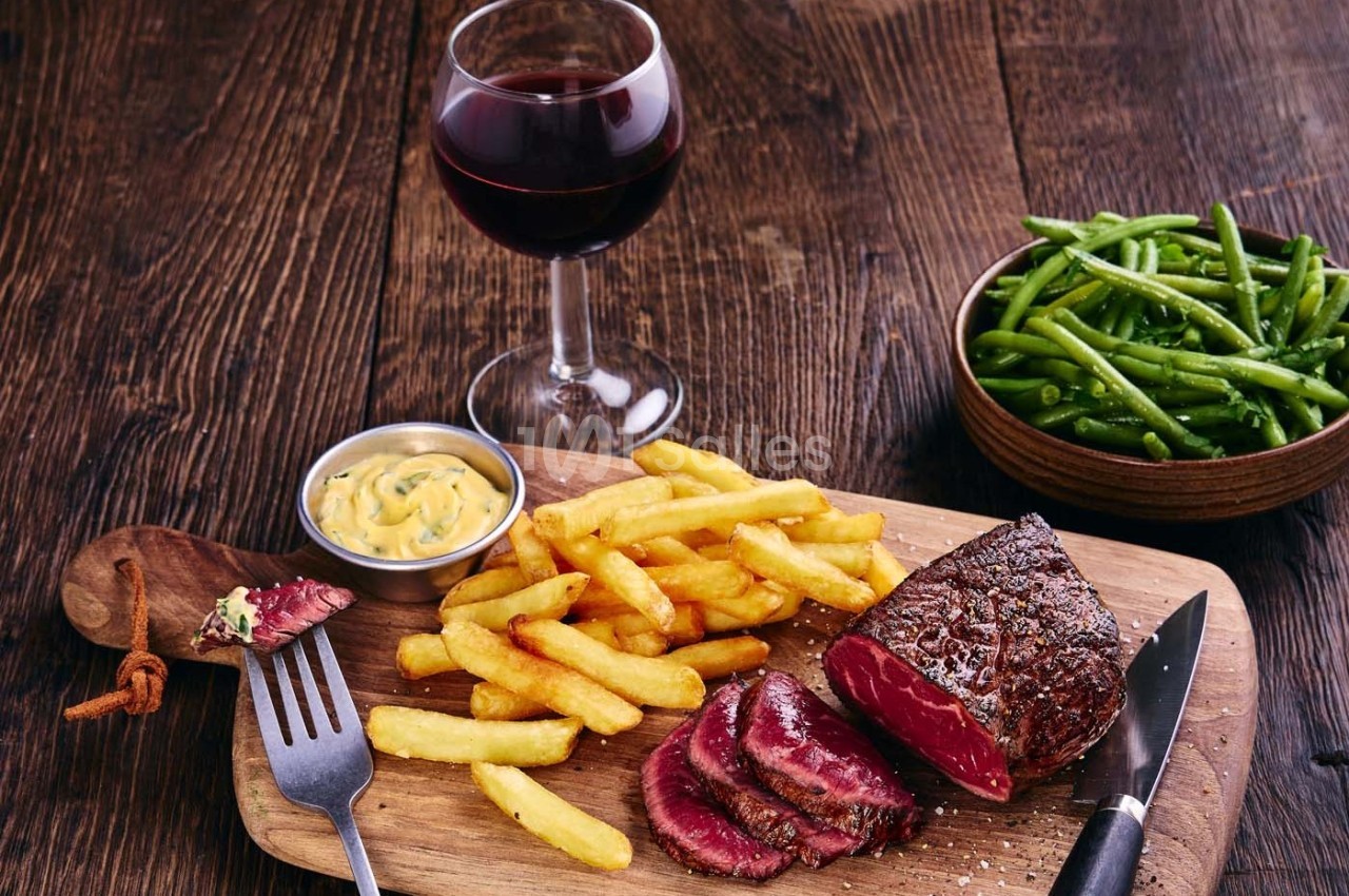 Assiette avec un steak saignant, des frites, une sauce, des haricots verts et un verre de vin rouge sur une table en bois.
