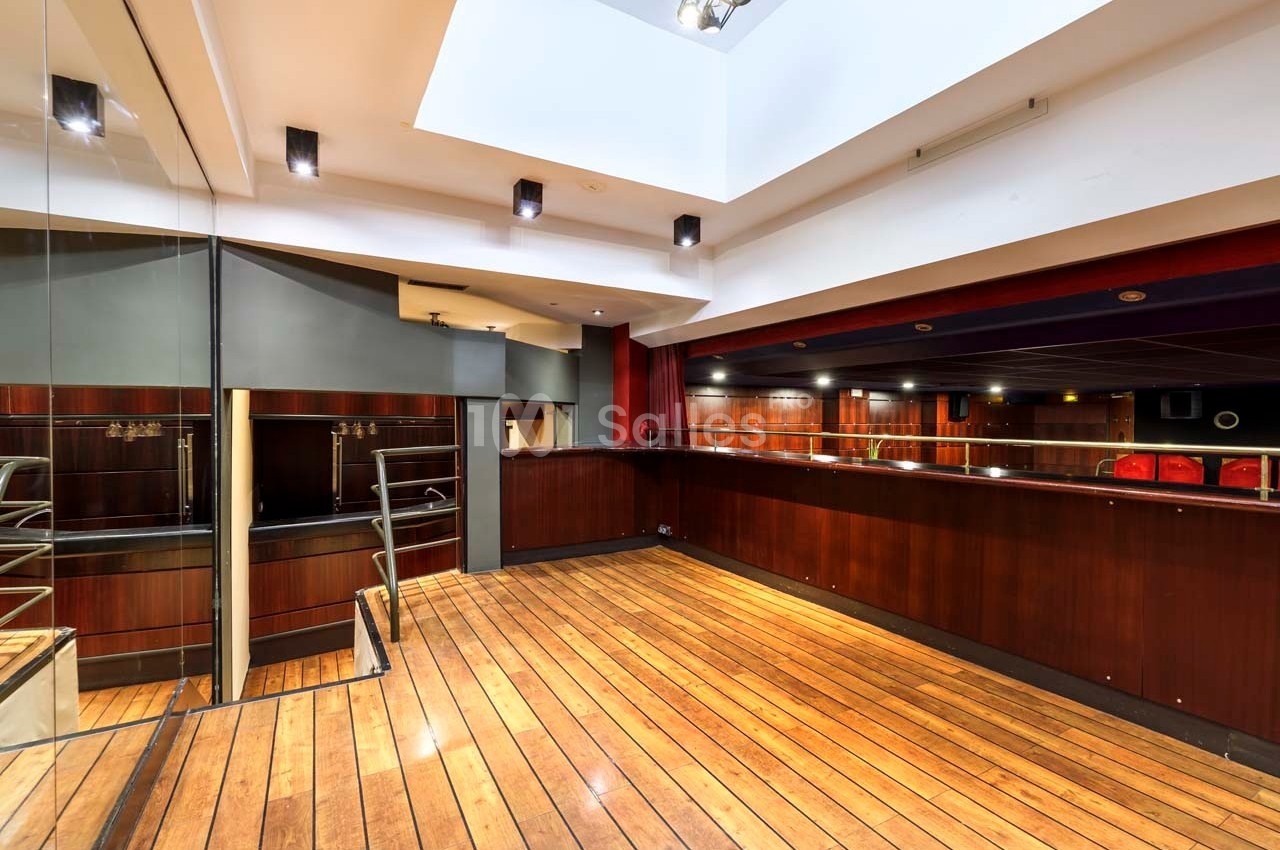 Salle intérieure avec parquet en bois, comptoir en bois sombre, murs clairs et éclairage encastré au plafond.