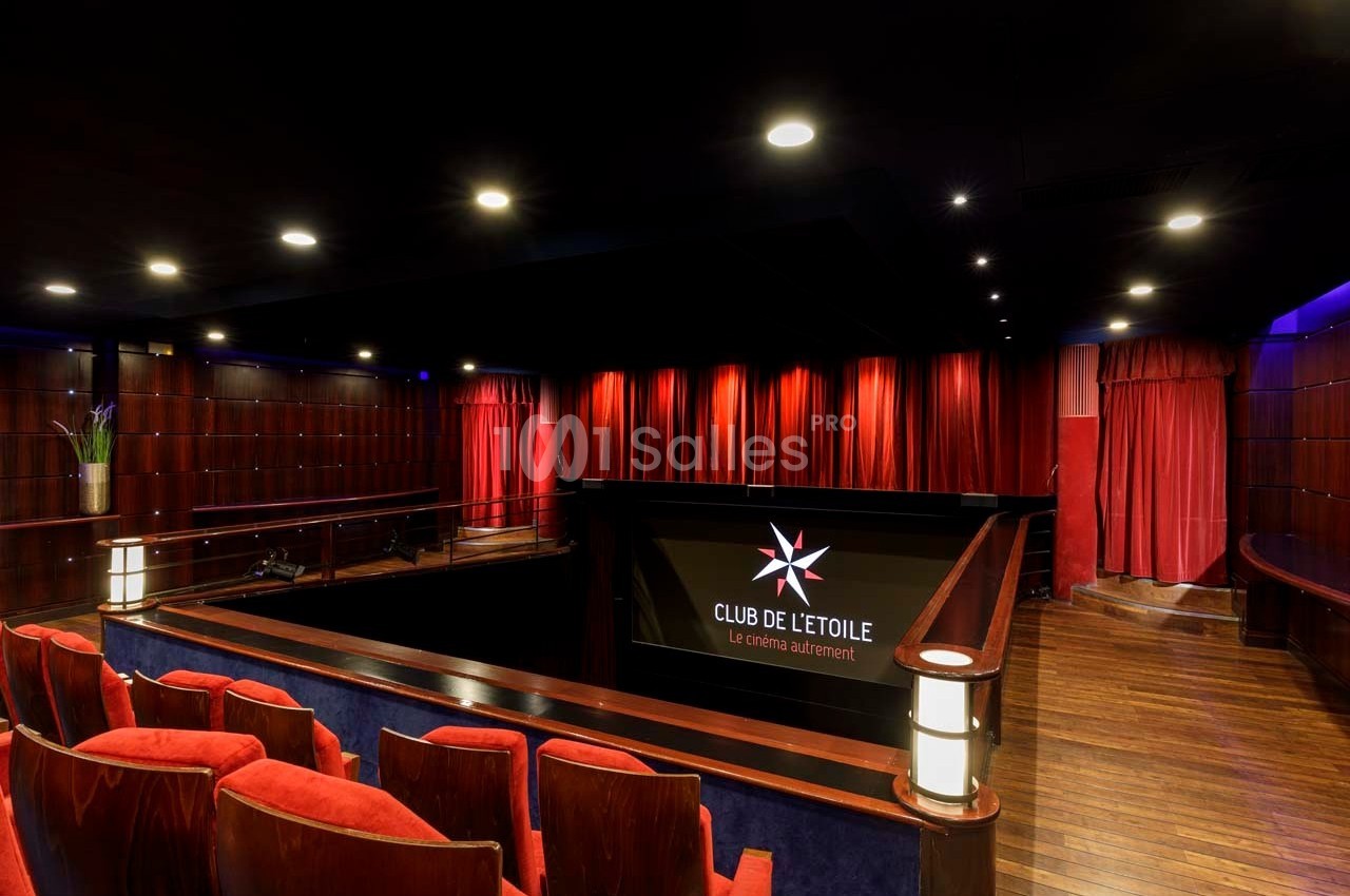 Salle de cinéma avec sièges rouges, rideaux rouges fermés et éclairage tamisé, vue depuis le balcon.