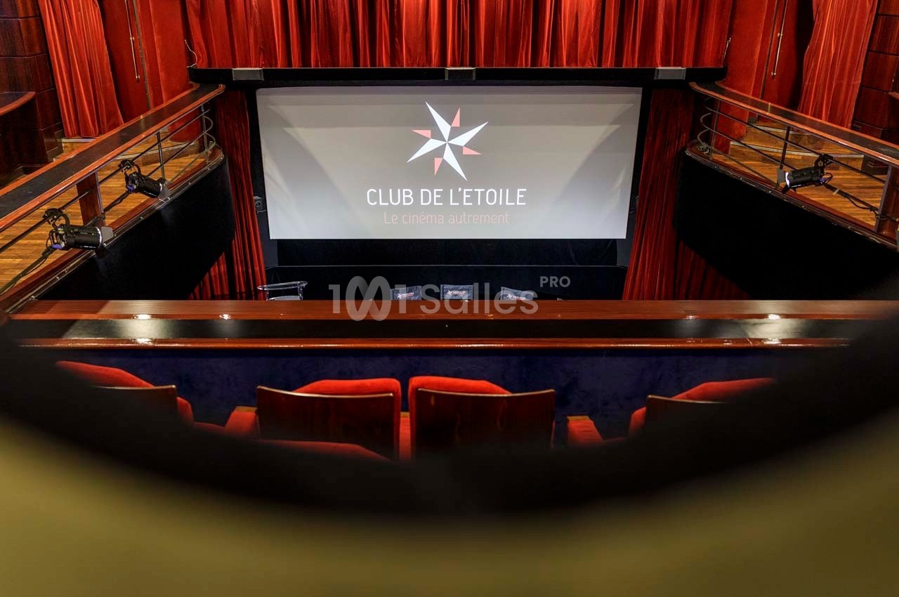 Salle de cinéma avec écran projetant le logo ’Club de l'Étoile’, vue depuis le balcon avec rideaux rouges.