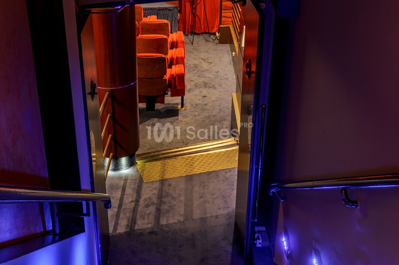 Entrée d'une salle de cinéma avec des sièges rouges visibles à travers une porte ouverte, éclairage tamisé.