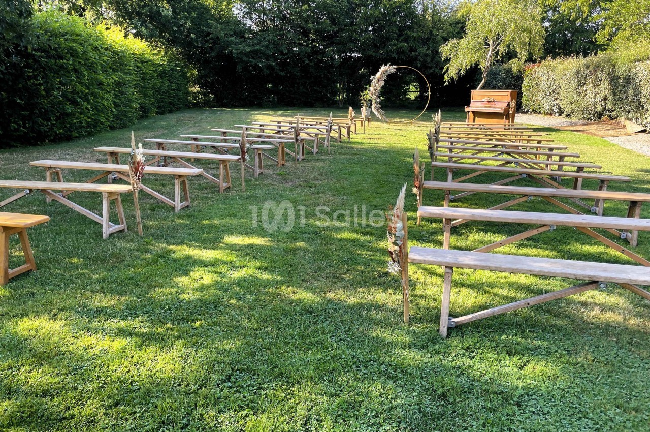Allée centrale avec bancs en bois disposés pour une cérémonie en plein air, entourée de verdure et d'un arche décoratif.