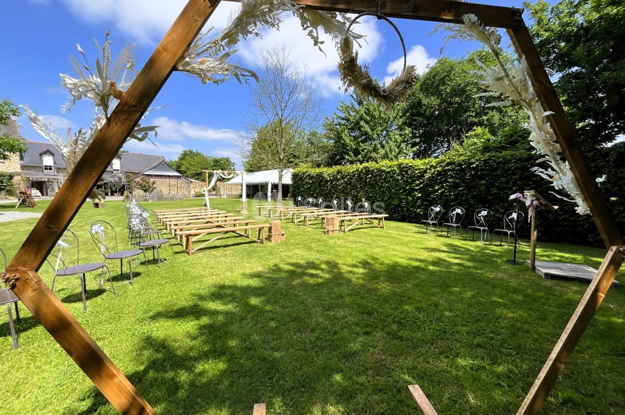 Arche en bois décorée, vue sur une cérémonie en plein air avec bancs, chaises et pelouse sous un ciel ensoleillé.