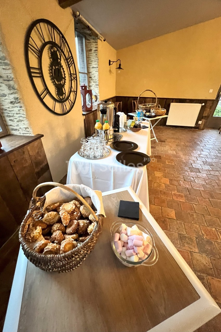 Buffet avec viennoiseries, boissons chaudes, jus d’orange et guimauves dans une salle au style rustique.