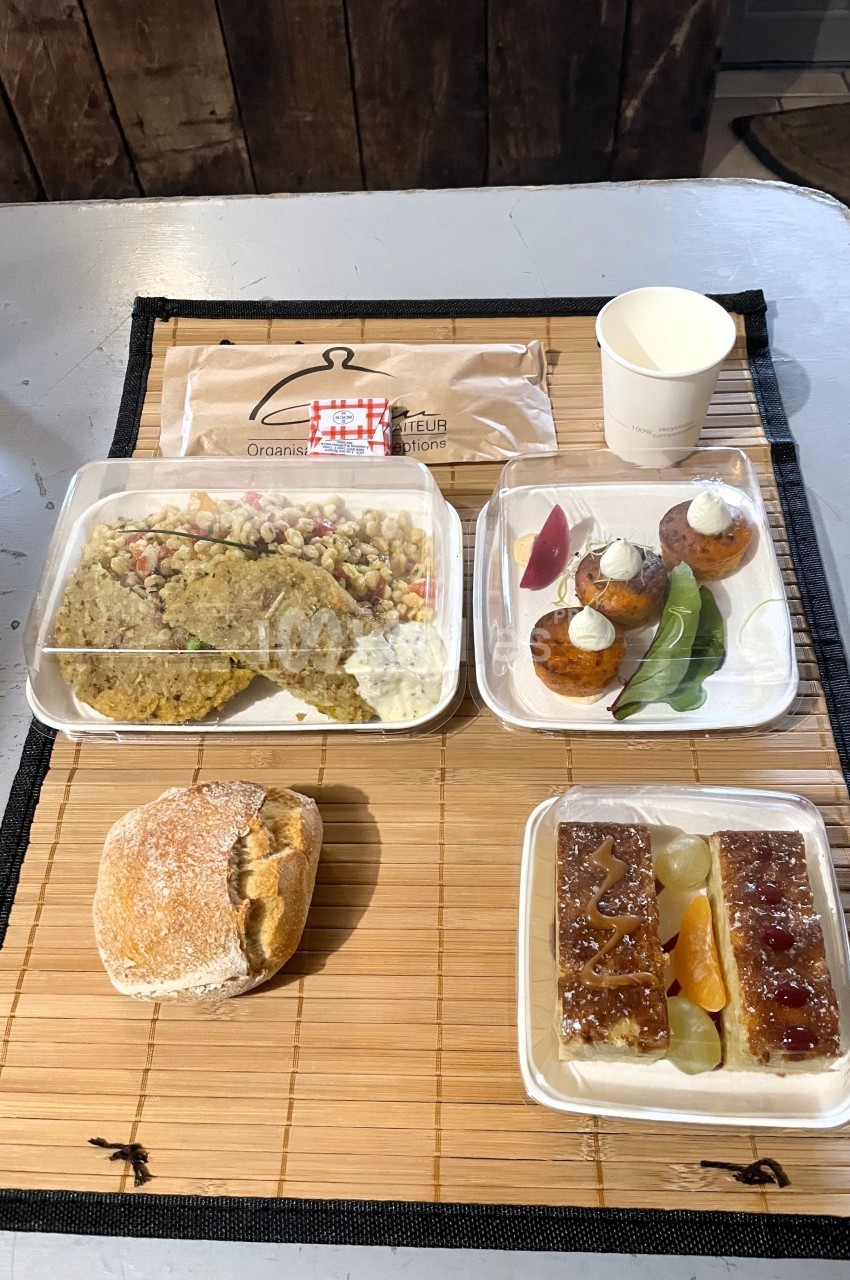 Repas composé de galettes, salade, pain, desserts variés et boisson, présenté sur un set en bambou.