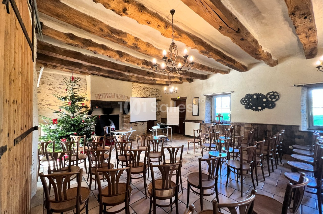 Salle de réunion rustique avec poutres apparentes, chaises en bois, sapin décoré et équipements de présentation.