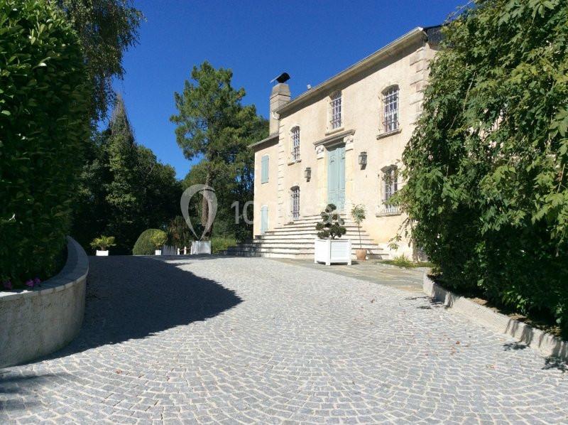 Allée pavée menant à une grande maison en pierre entourée de végétation sous un ciel bleu.