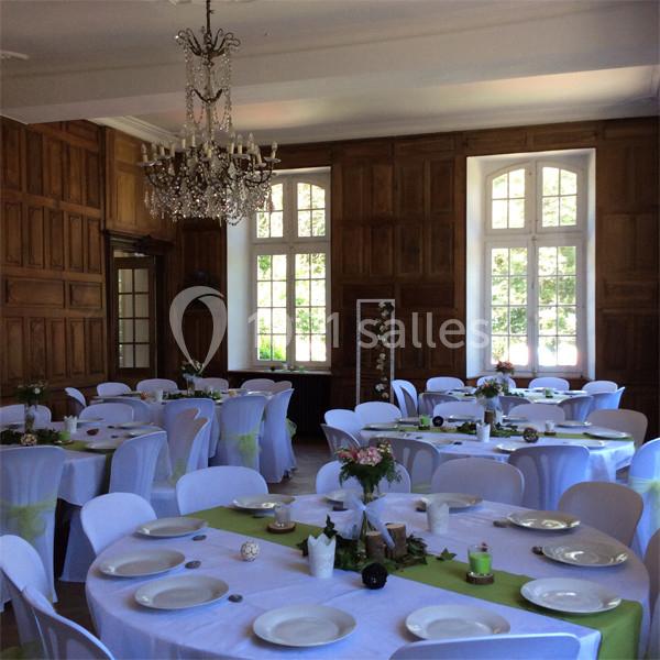 Salle de réception lumineuse avec tables rondes dressées, nappes blanches et décorations florales.