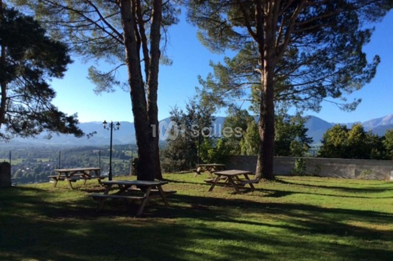 Tables de pique-nique en bois disposées sur une pelouse ombragée, avec vue sur des montagnes et un ciel dégagé.