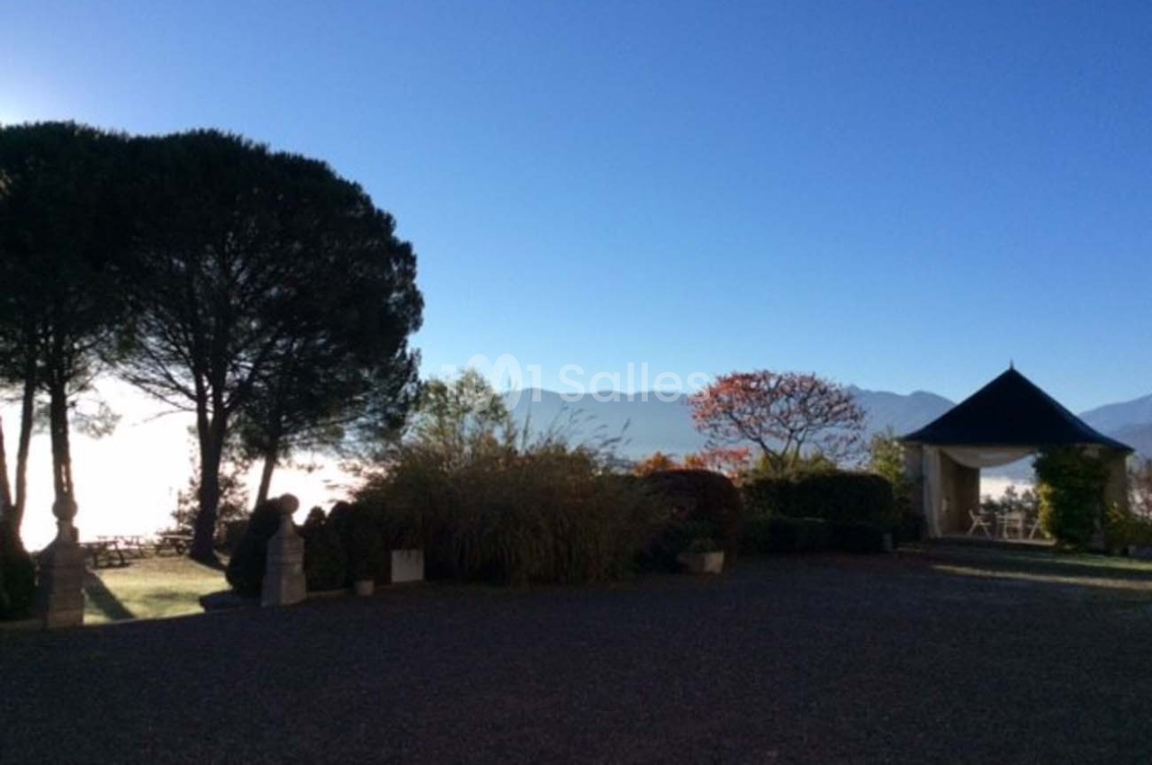 Cour avec vue sur des arbres, un kiosque et des montagnes en arrière-plan sous un ciel bleu clair.