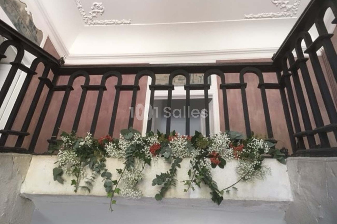 Guirlande de feuillage et fleurs blanches et rouges suspendue à une rambarde en bois dans un intérieur lumineux.