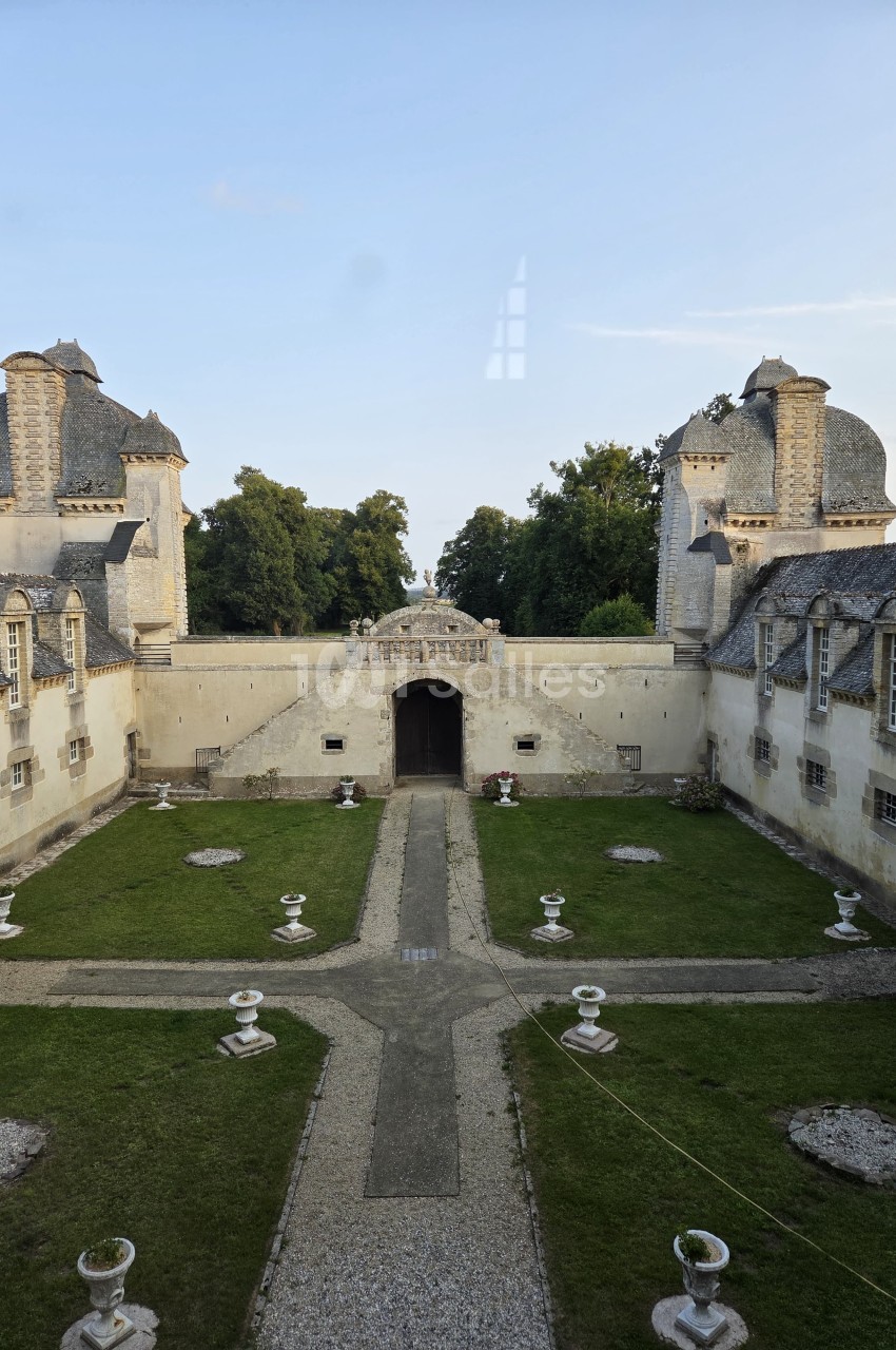 Cour intérieure d'un château avec pelouse, allées gravillonnées, fontaines décoratives et bâtiments en pierre.