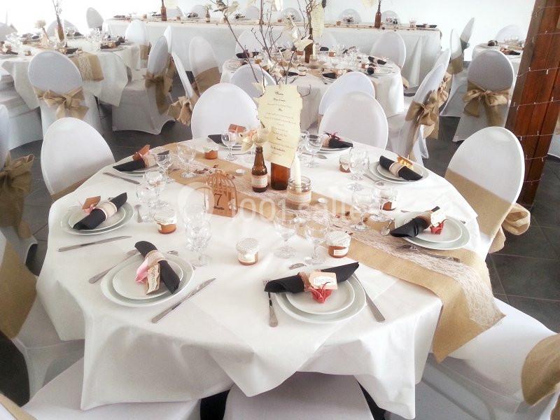 Table décorée pour un mariage avec nappes blanches, chemins de table en jute, vaisselle élégante et centres de table…