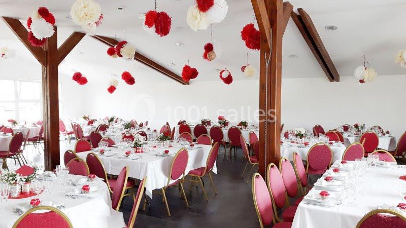 Salle de réception décorée de pompons rouges et blancs, avec des tables rondes dressées et des chaises rouges.