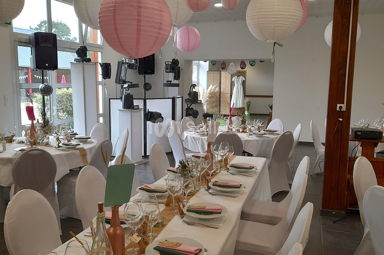 Salle décorée pour un événement avec des tables dressées, des lanternes suspendues et une robe exposée en arrière-plan.