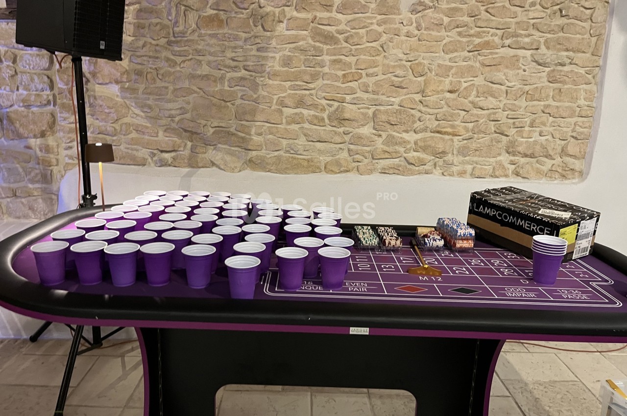 Table de jeu avec des gobelets violets alignés, des jetons de casino et une boîte posée sur une nappe violette.