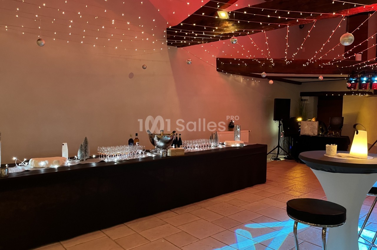 Table de réception décorée avec des guirlandes lumineuses, verres alignés et ambiance tamisée dans une salle festive.