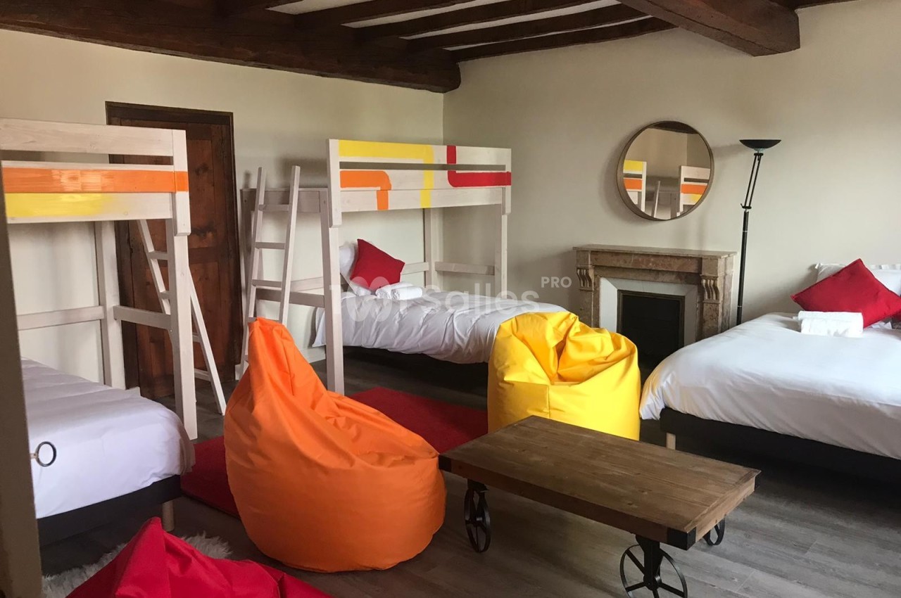 Chambre avec lits superposés, lit double, poufs colorés, table basse en bois et cheminée décorative.