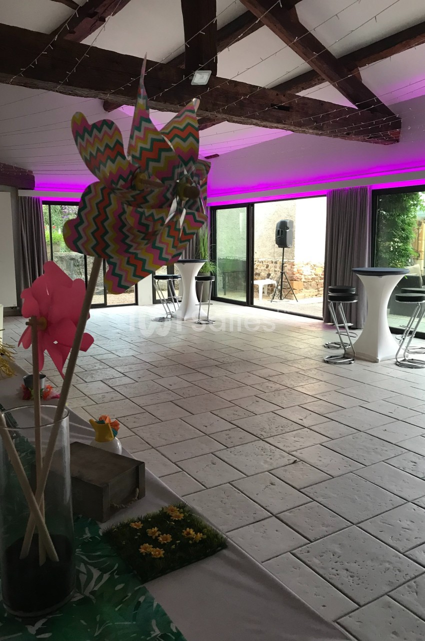 Salle lumineuse avec grandes baies vitrées, décoration colorée et mobilier moderne sous un plafond avec poutres apparentes.