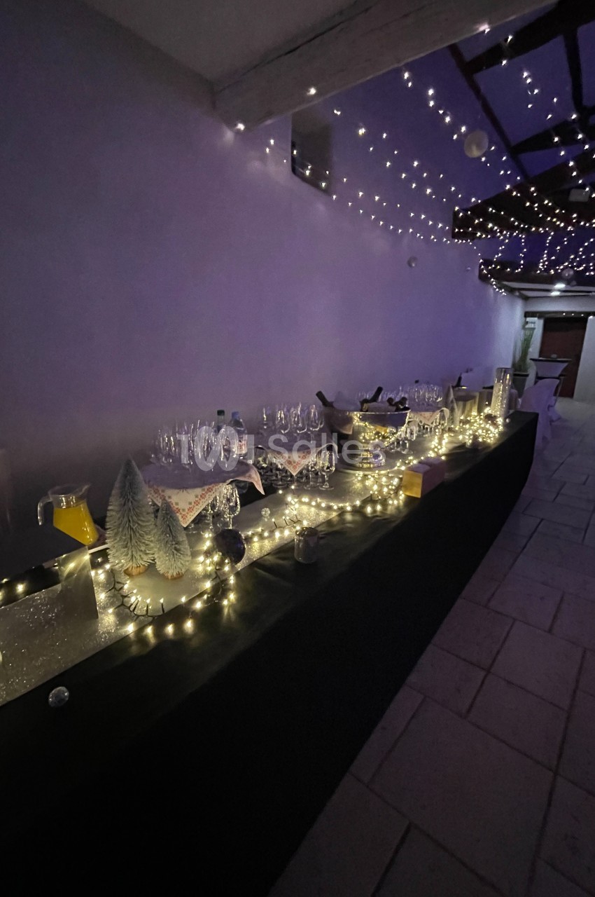 Table décorée avec guirlandes lumineuses, verres et carafes, dans un espace couvert avec éclairage tamisé.