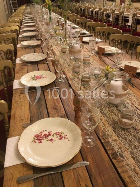 Table en bois décorée pour un repas, avec assiettes fleuries, verres, couverts et chemins de table en dentelle.
