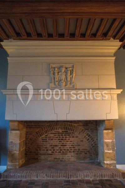 Cheminée ancienne en pierre avec un bas-relief sculpté, encadrée par un mur bleu et un plafond en bois.