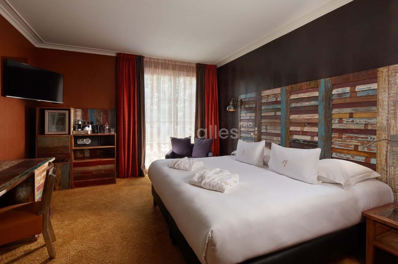 Chambre d'hôtel avec lit double, bureau, télévision murale, fauteuils, et décoration aux tons chauds et boisés.
