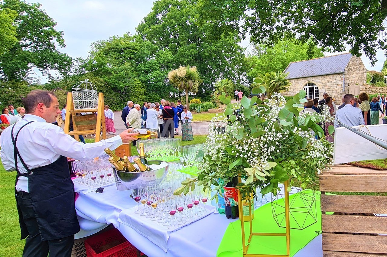 Serveur préparant des boissons sur une table dressée en extérieur lors d'un événement convivial dans un jardin.