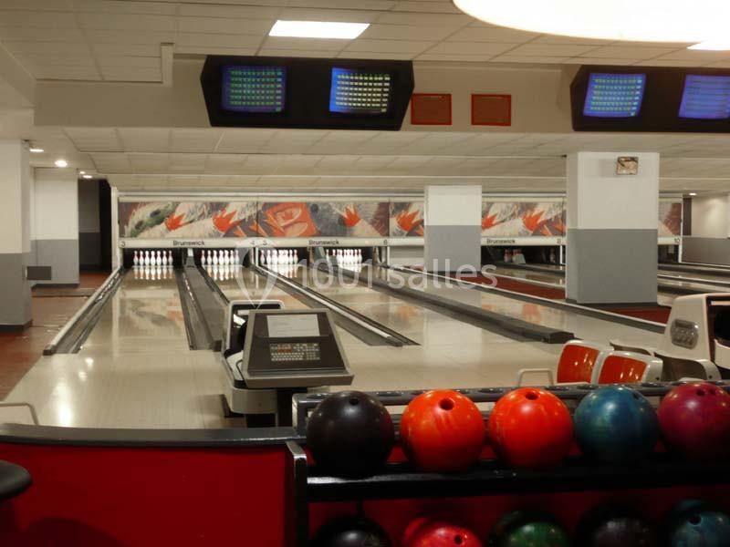 Salle de bowling avec plusieurs pistes alignées, des écrans d'affichage et des boules colorées au premier plan.