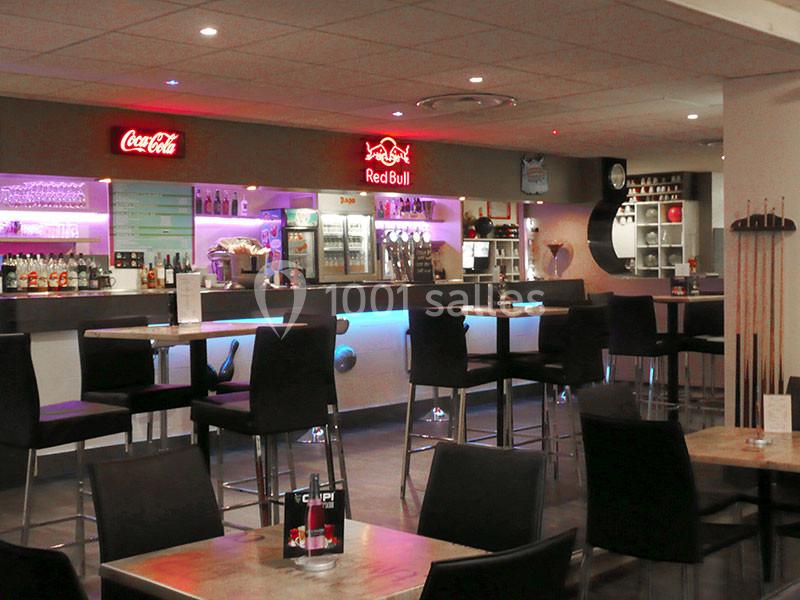 Bar moderne avec comptoir éclairé, tabourets hauts, tables en bois et enseignes lumineuses de boissons.