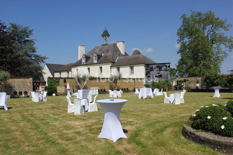 Jardin avec tables hautes et chaises blanches disposées pour un événement en extérieur devant un bâtiment ancien.