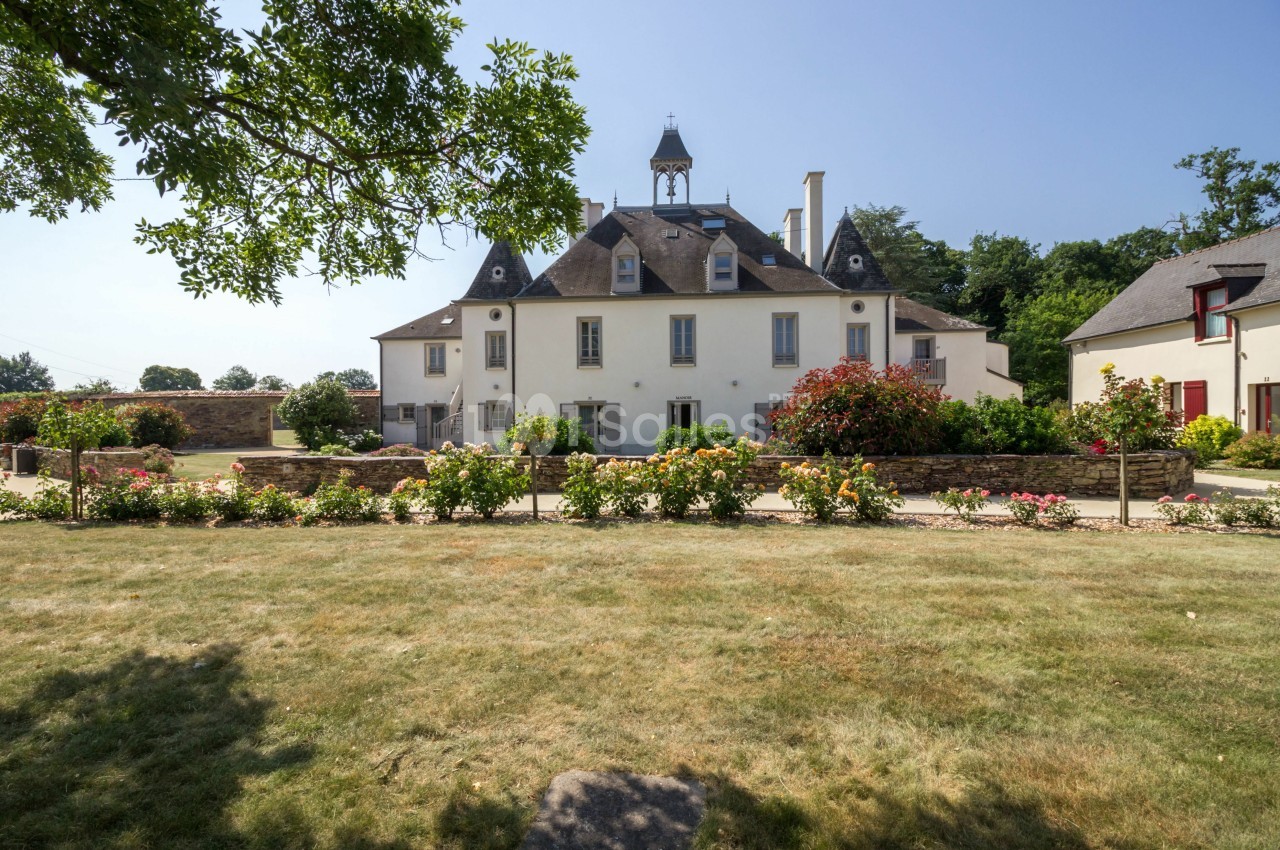 Grande maison de style traditionnel avec un jardin fleuri, vue dégagée sous un ciel bleu.