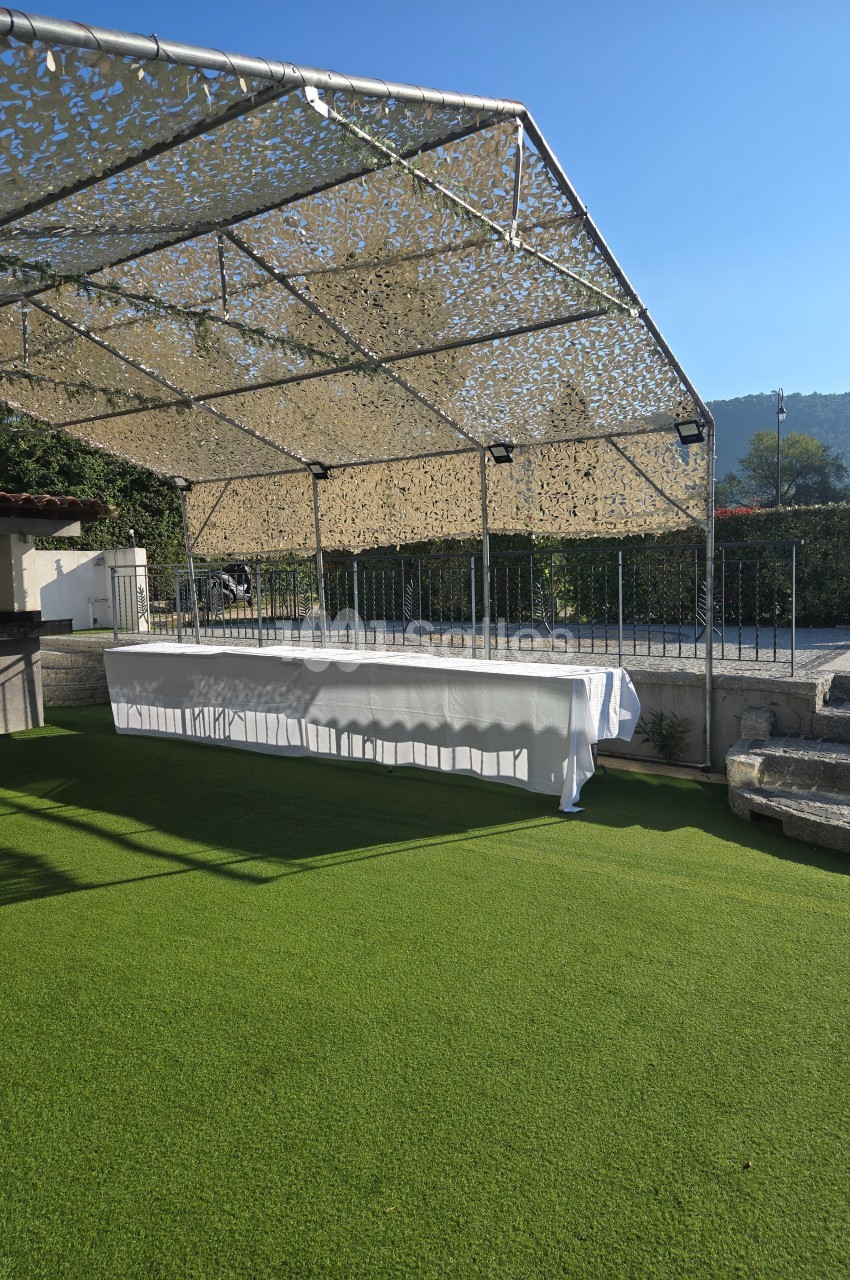 Table drapée de blanc sous une structure ombragée, installée sur une pelouse synthétique par temps ensoleillé.
