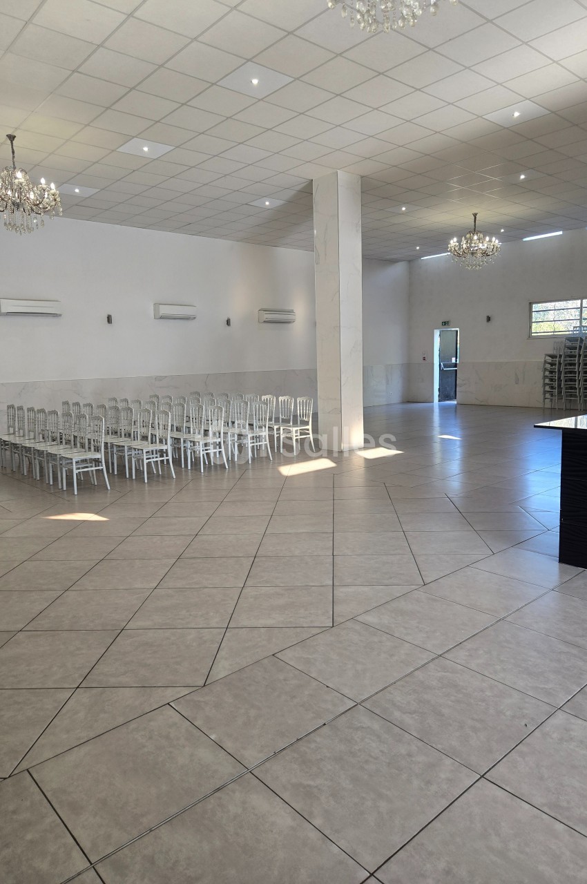 Salle spacieuse avec carrelage clair, chaises alignées sur le côté, lustres suspendus et lumière naturelle.
