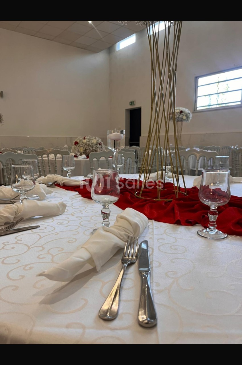 Table de réception élégamment dressée avec nappes blanches, serviettes pliées, couverts, verres et décoration florale.