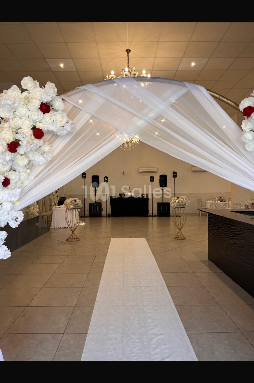 Allée centrale décorée de fleurs blanches et rouges, menant à une scène avec des équipements audio dans une salle de…