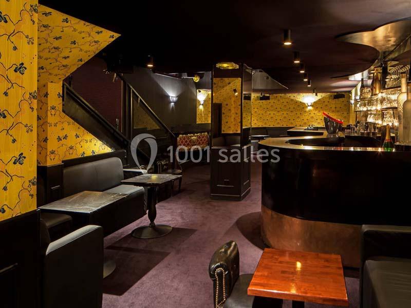 Intérieur d'un bar élégant avec mobilier sombre, murs jaunes à motifs et éclairage tamisé.
