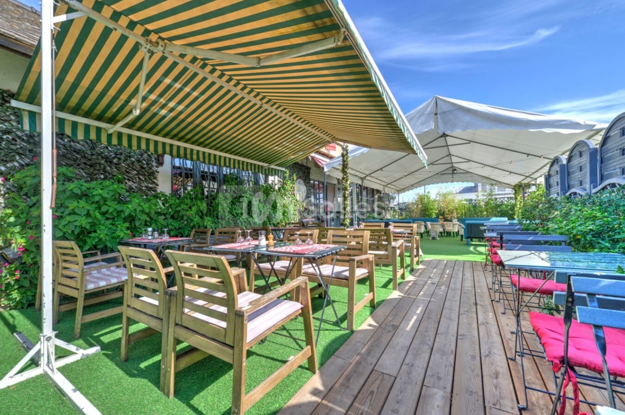 Terrasse extérieure avec tables et chaises en bois sous des auvents, entourée de verdure et de ciel dégagé.