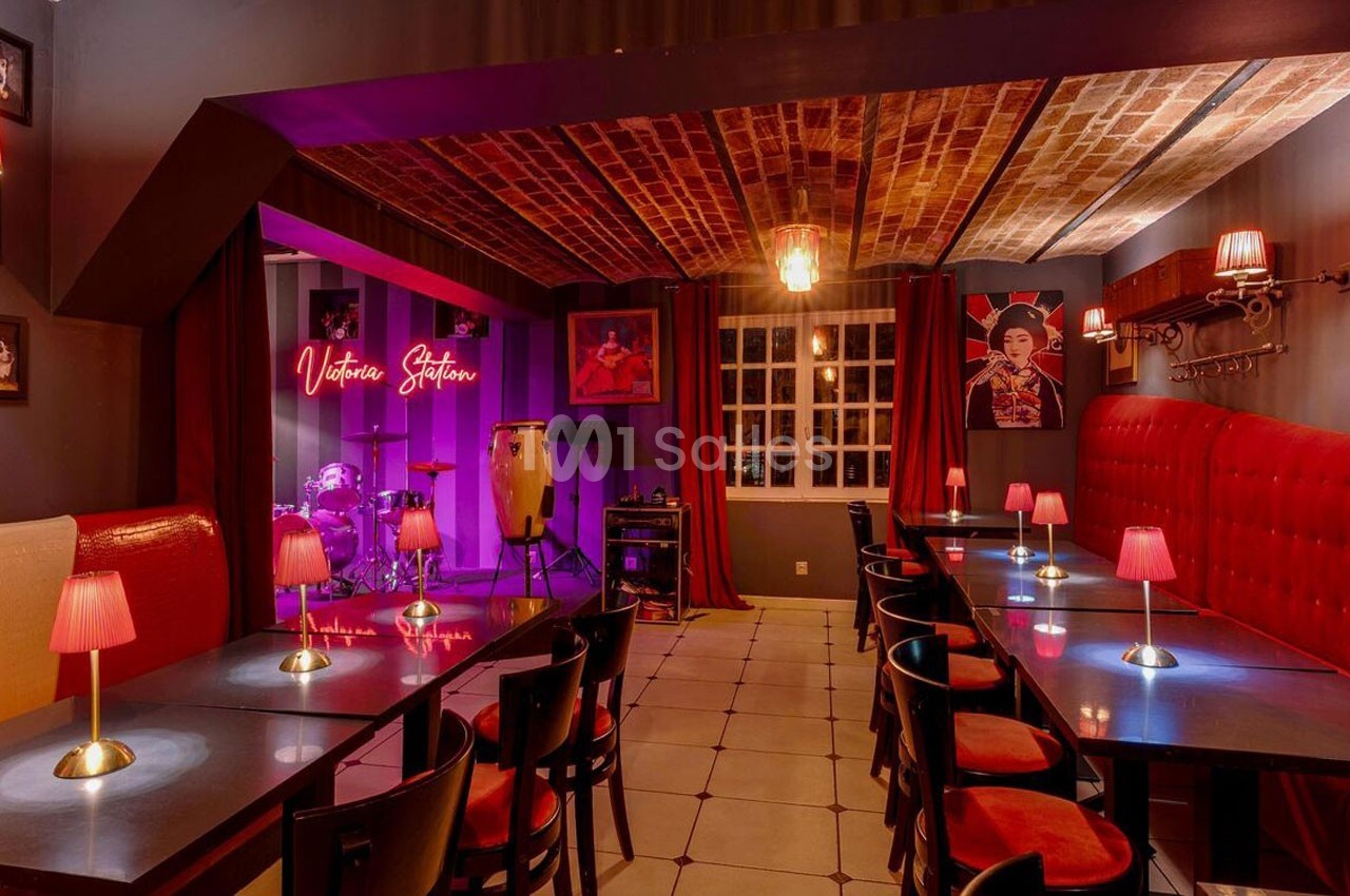 Salle de restaurant avec tables, chaises, éclairage tamisé et une scène équipée d'instruments de musique.