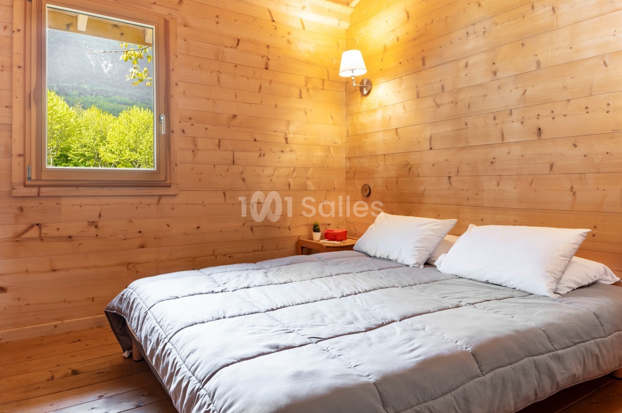 Chambre en bois avec un lit double, une lampe murale allumée et une fenêtre offrant une vue sur la montagne.