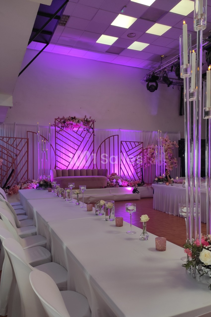Salle de réception décorée avec des tons roses et violets, tables dressées et bougies hautes illuminées.