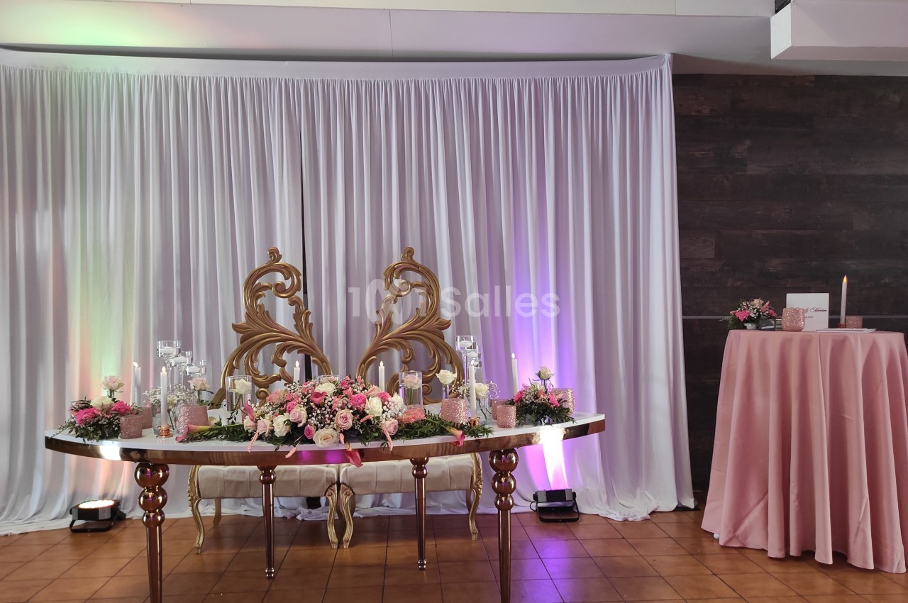 Table décorée avec des fleurs roses, bougies et ornements dorés devant un rideau blanc et un mur sombre.