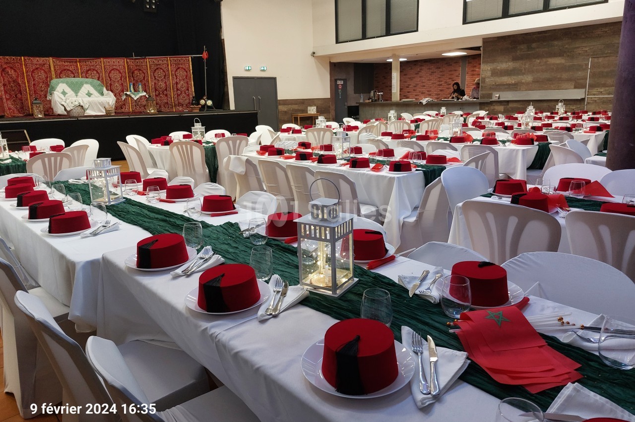 Salle décorée pour un événement avec tables alignées, nappes blanches, lanternes et chapeaux rouges en guise de décoration.