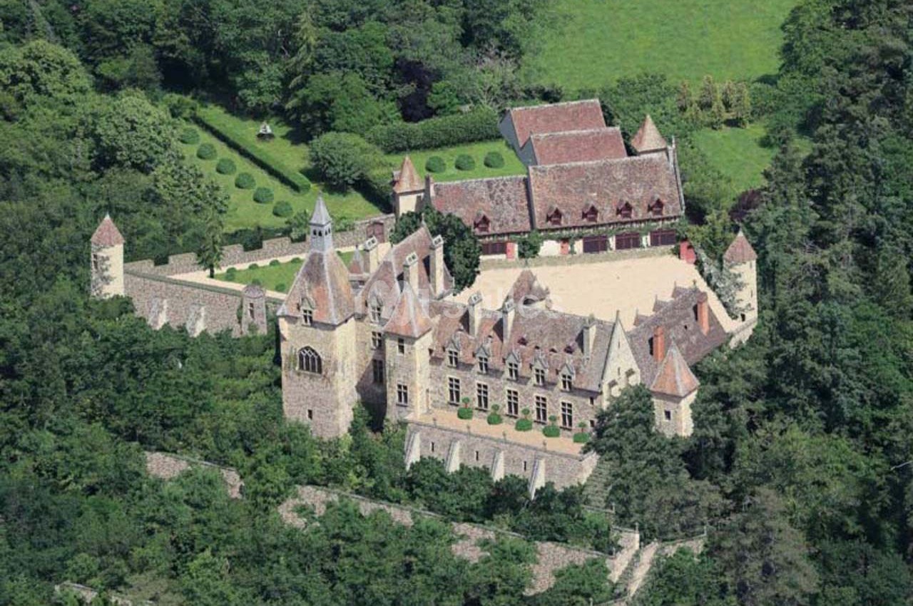 Vue aérienne d'un château médiéval entouré de jardins, de forêts et de bâtiments annexes avec toits en tuiles.