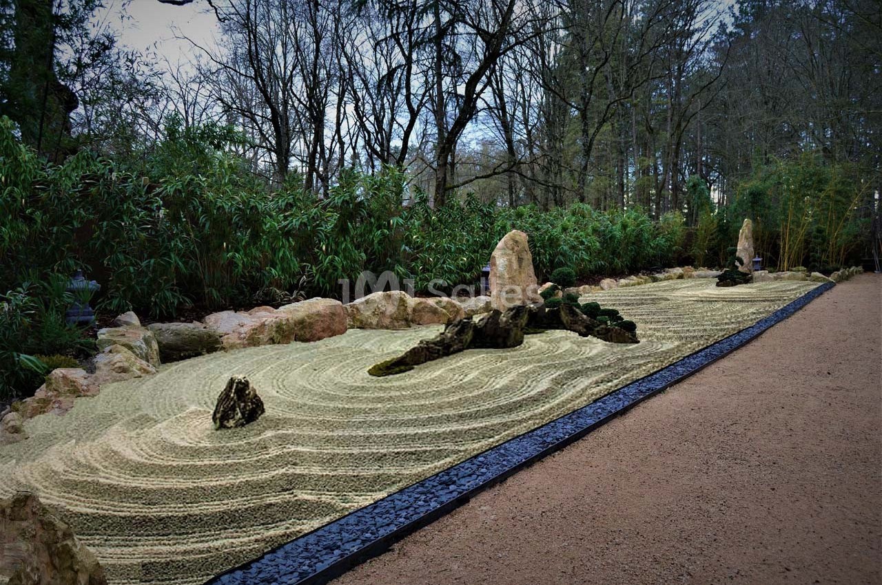 Jardin zen avec gravier ratissé en motifs ondulés, pierres disposées harmonieusement et végétation en arrière-plan.